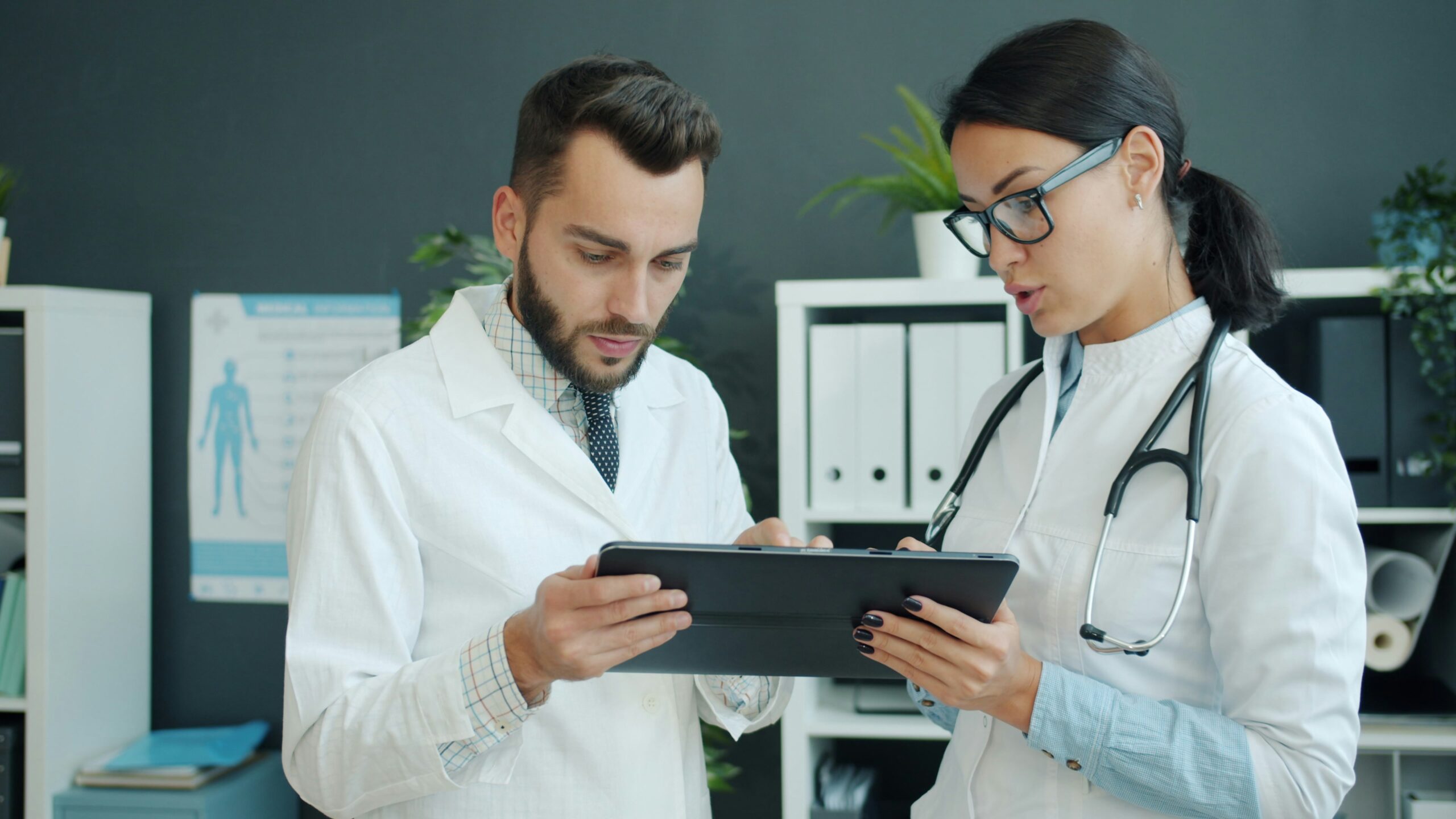 Two doctors discuss a patient's file over a tablet device.